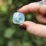 Someone holding the Opalite Crystal Tumble in front of a blurry green background.