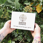 Someone holding the Opalite Crystal Facial Roller Set in front of a green bush.