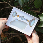 Someone holding the Opalite Crystal Facial Roller Set in front of a green bush.