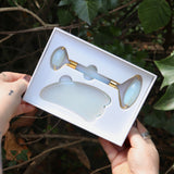 Someone holding the Opalite Crystal Facial Roller Set in front of a green bush.