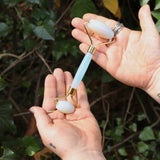 Someone holding the roller from the Opalite Crystal Facial Roller Set in front of a green bush.