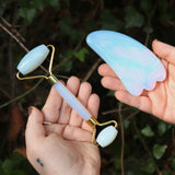 Someone holding the Opalite Crystal Facial Roller Set in front of a green bush.