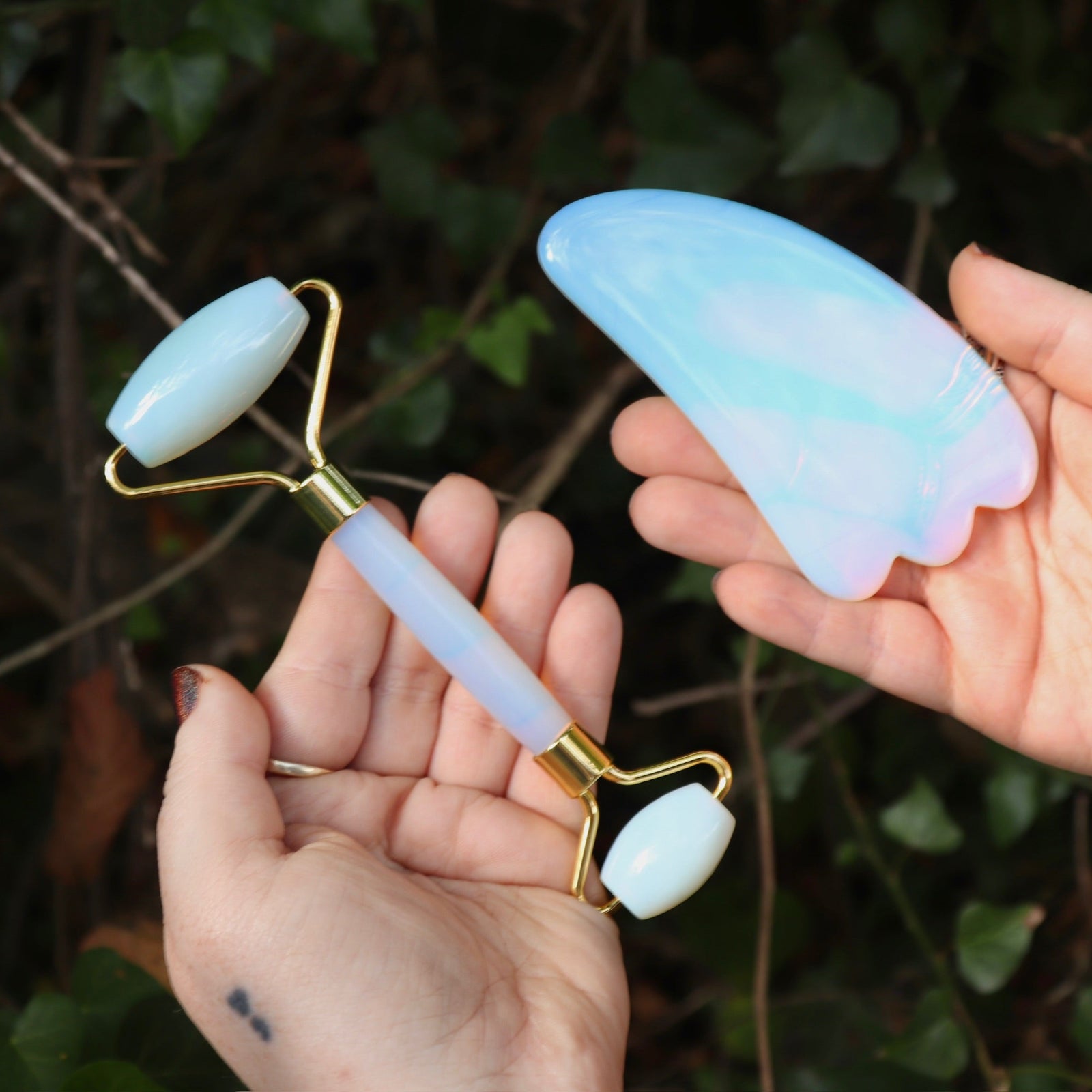Someone holding the Opalite Crystal Facial Roller Set in front of a green bush.