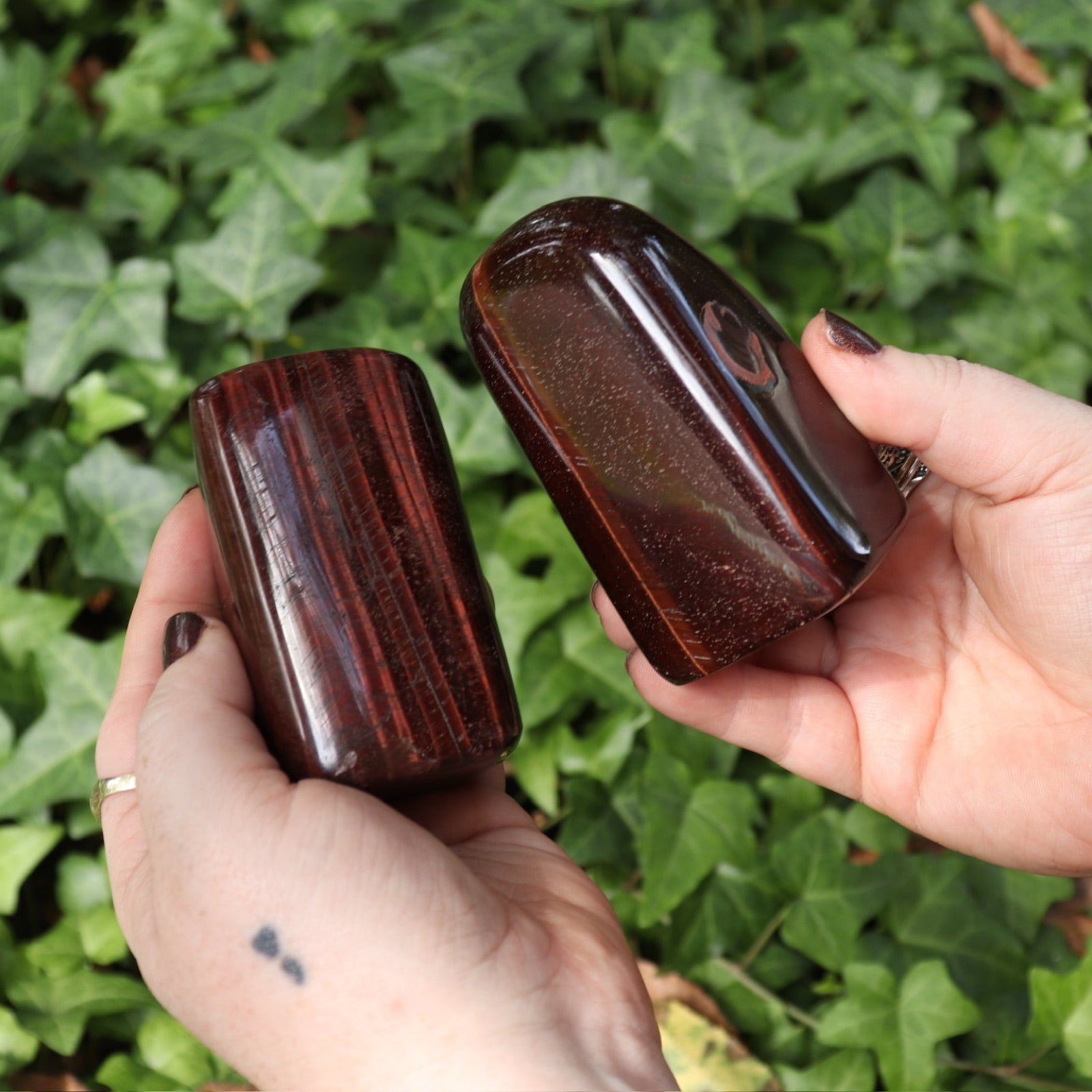 Someone holding two of the Red Tiger's Eye Freeform pieces in front of a green nature background.
