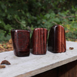 Three of the Red Tiger's Eye Freeform pieces on a wooden slab in front of a green nature background.