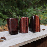 Three of the Red Tiger's Eye Freeform pieces on a wooden slab in front of a green nature background.