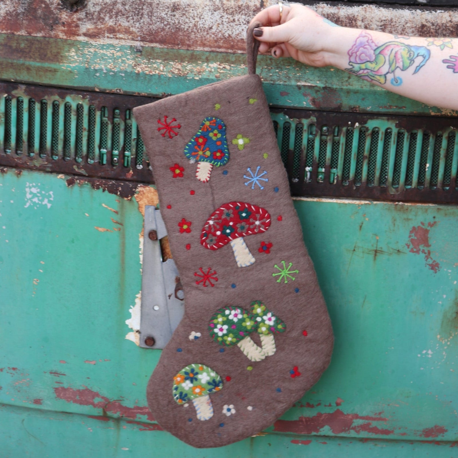 Someone holding the Handmade Gray Mushroom Felt Boho Stocking in front of a vintage teal Volkswagen bus.