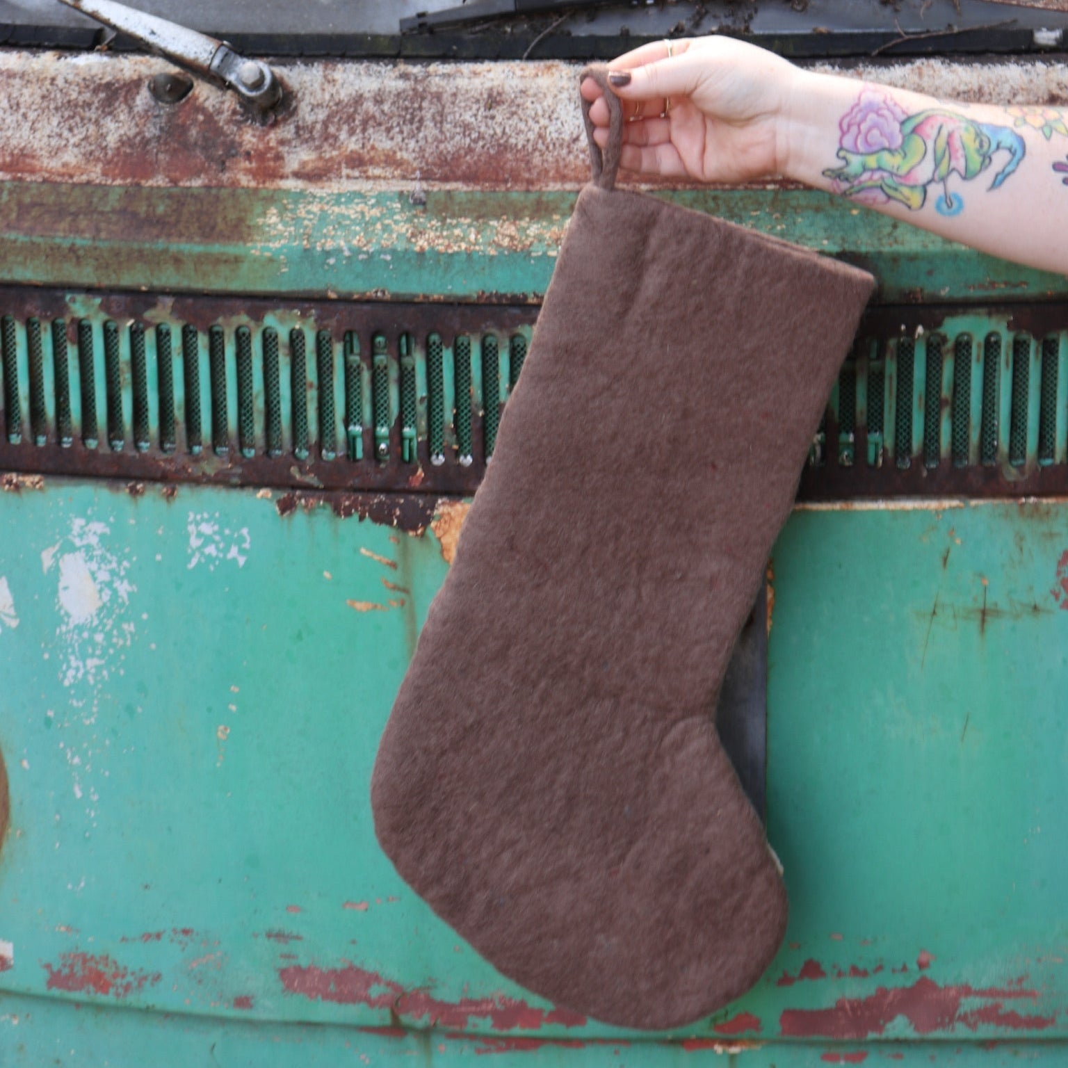 Someone holding the Handmade Gray Mushroom Felt Boho Stocking in front of a vintage teal Volkswagen bus, showing off the back.