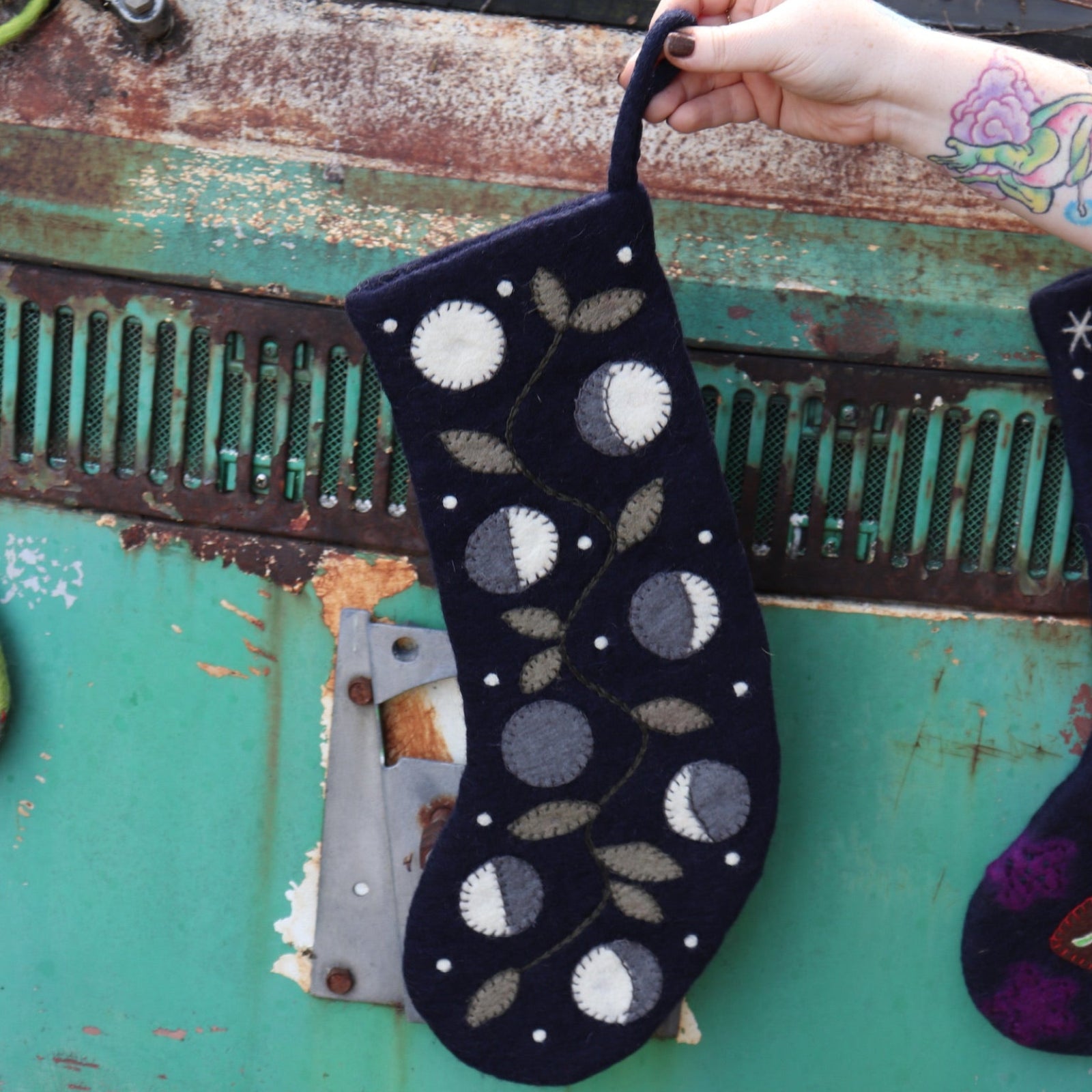 Someone holding the Moon Cycle Felt Celestial Holiday Stocking in front of a vintage teal Volkswagen bus.
