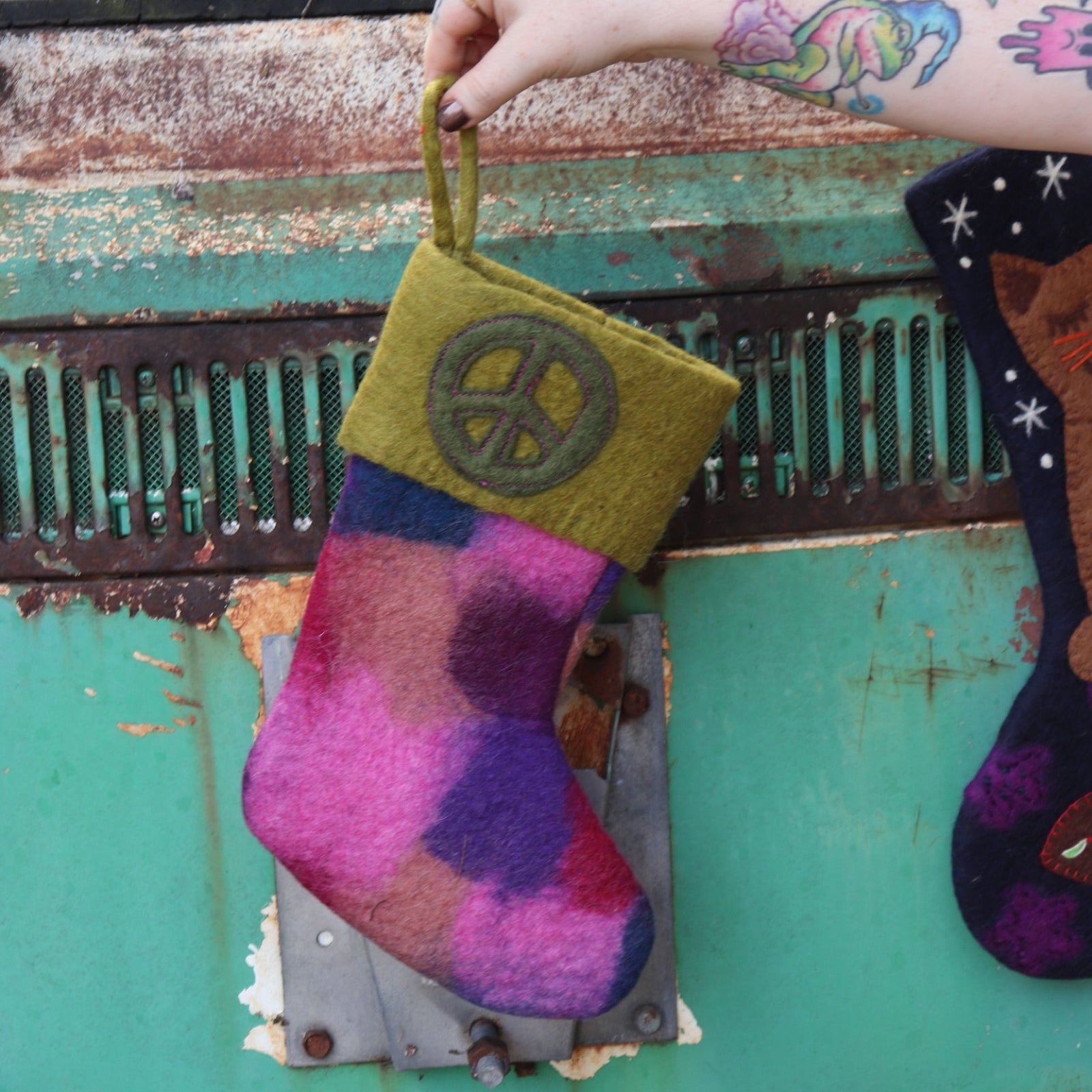 Someone holding the olive Tie-Dye Peace Pure Wool Felt Handcrafted Stocking in front of a vintage teal Volkswagen bus.