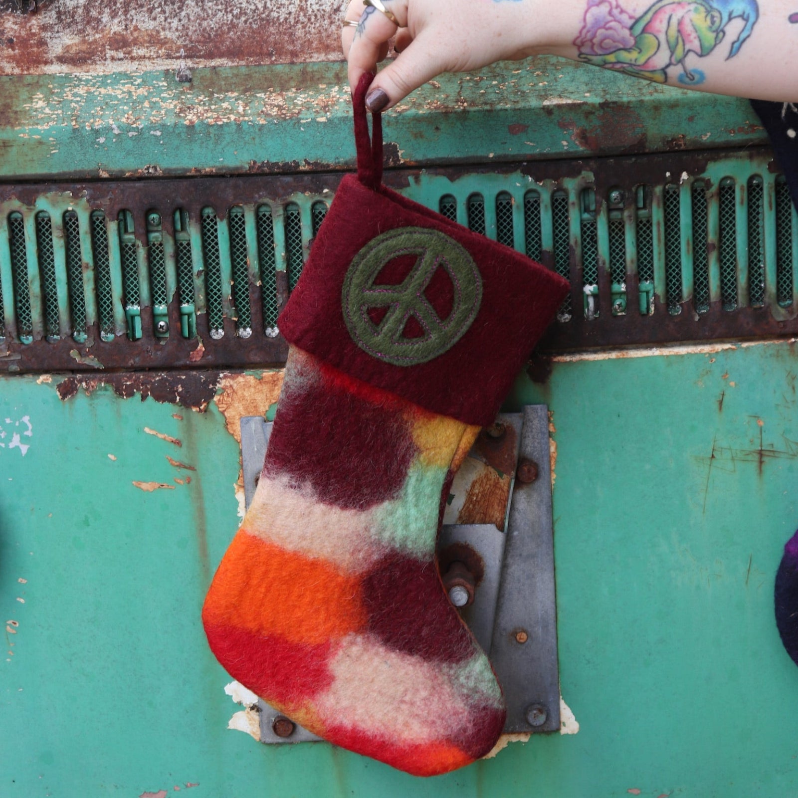 Someone holding the burgundy Tie-Dye Peace Pure Wool Felt Handcrafted Stocking in front of a vintage teal Volkswagen bus.