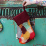 Someone holding the burgundy Tie-Dye Peace Pure Wool Felt Handcrafted Stocking in front of a vintage teal Volkswagen bus, showing off the back.