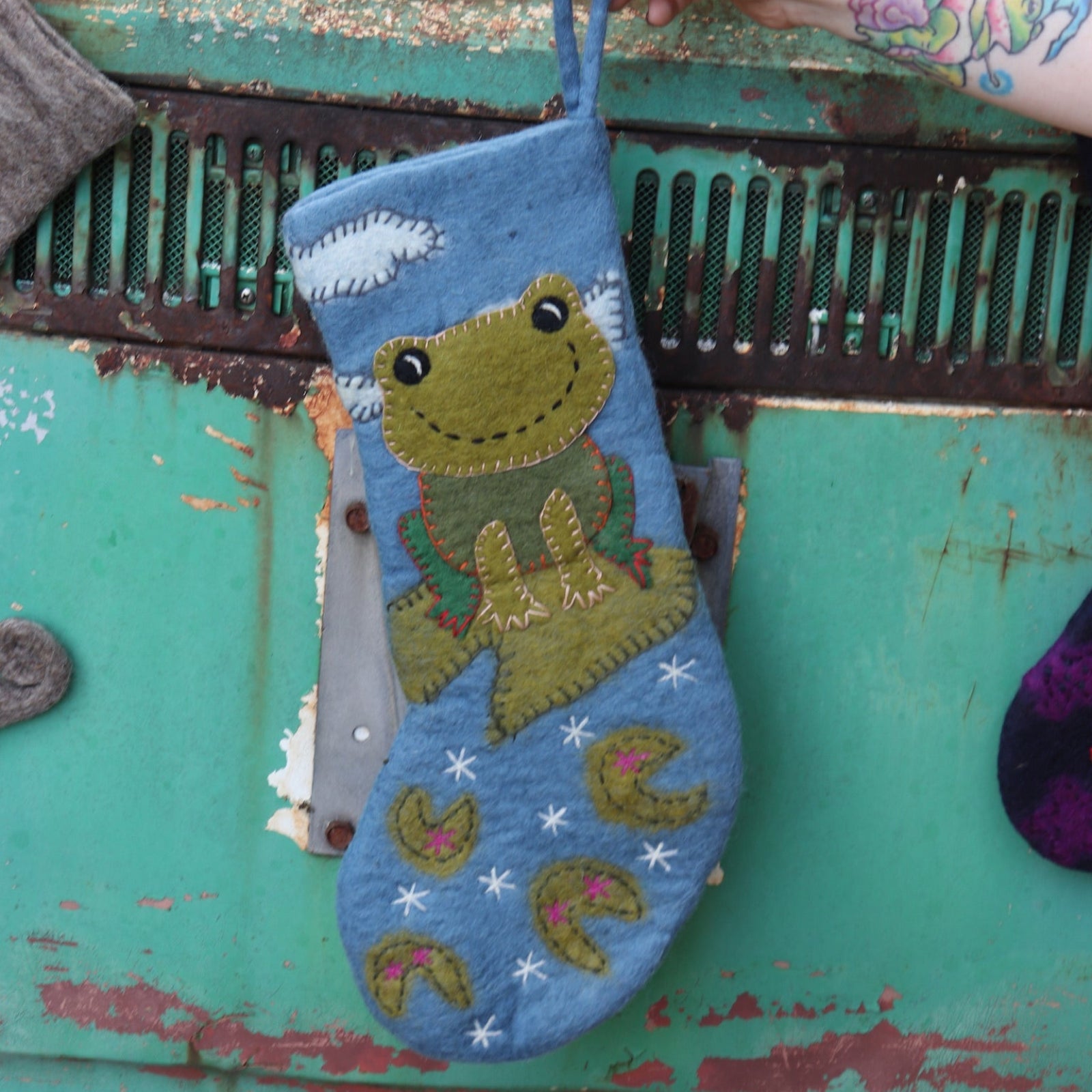 Someone holding the frog Folk Art Embroidered Pure Wool Felt Handcrafted Stocking in front of a vintage teal Volkswagen bus.