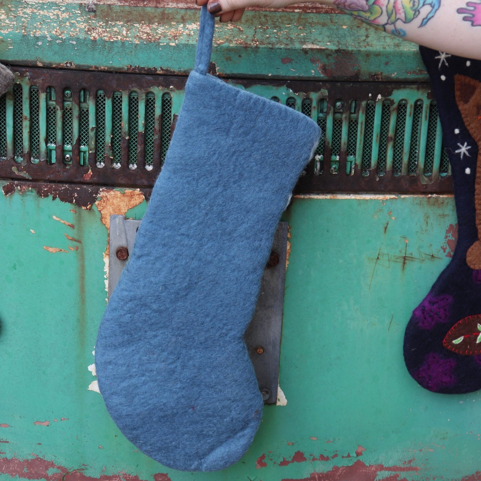 Someone holding the frog Folk Art Embroidered Pure Wool Felt Handcrafted Stocking in front of a vintage teal Volkswagen bus, showing off the back.