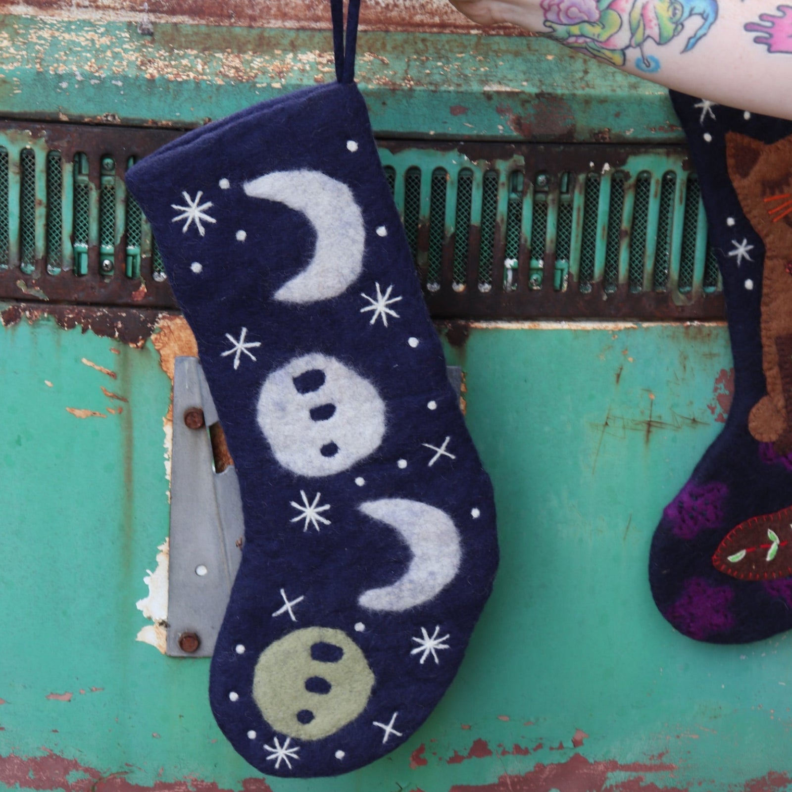 Someone holding the Mystical Moon Phase Felt Holiday Pure Wool Handcrafted Stocking in front of a vintage teal Volkswagen bus.