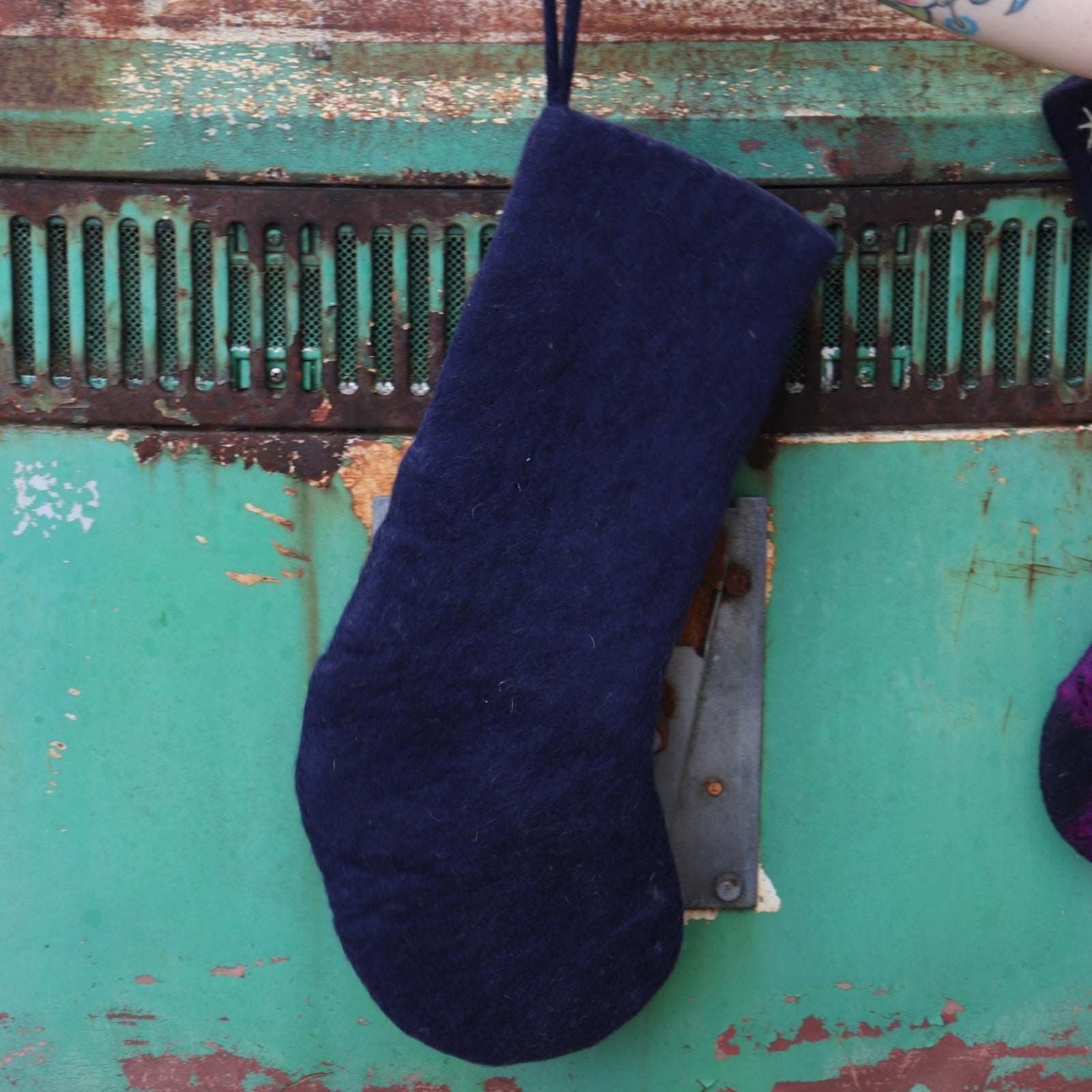 Someone holding the Mystical Moon Phase Felt Holiday Pure Wool Handcrafted Stocking in front of a vintage teal Volkswagen bus, showing off the back.