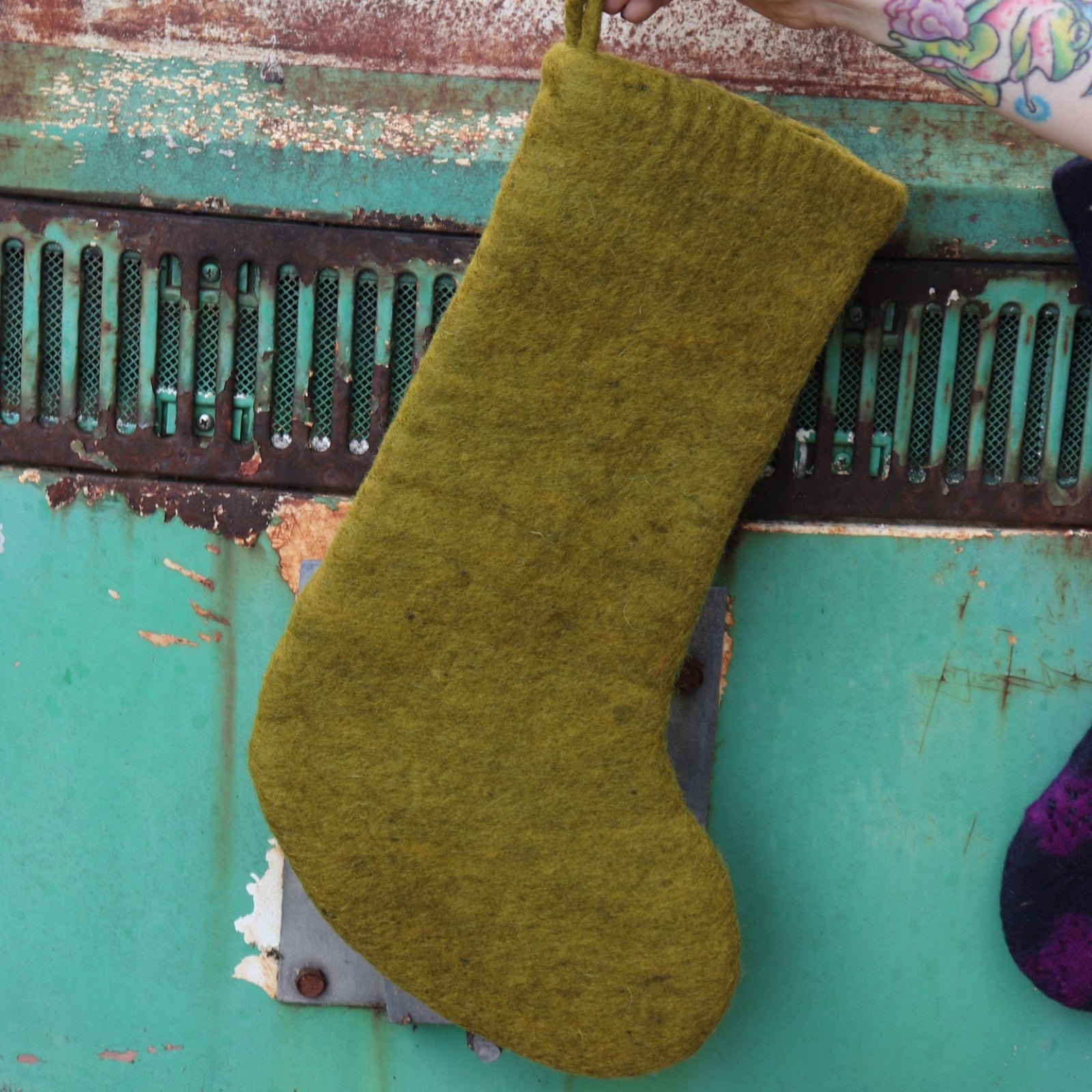Someone holding the Tree of Life Mystical Felt Stocking in front of a vintage teal Volkswagen bus, showing off the back.