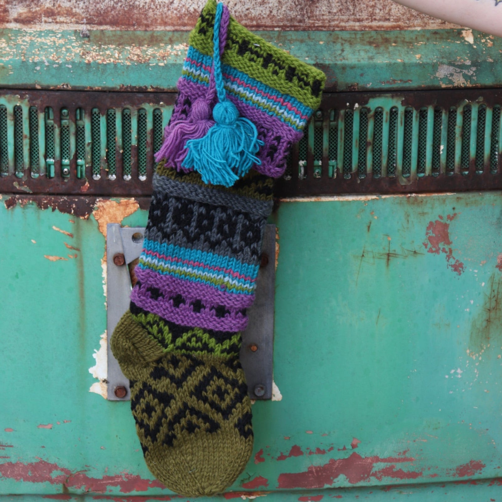Someone holding up the Wool Handcrafted Diamond Stocking in front of a vintage teal Volkswagen bus.