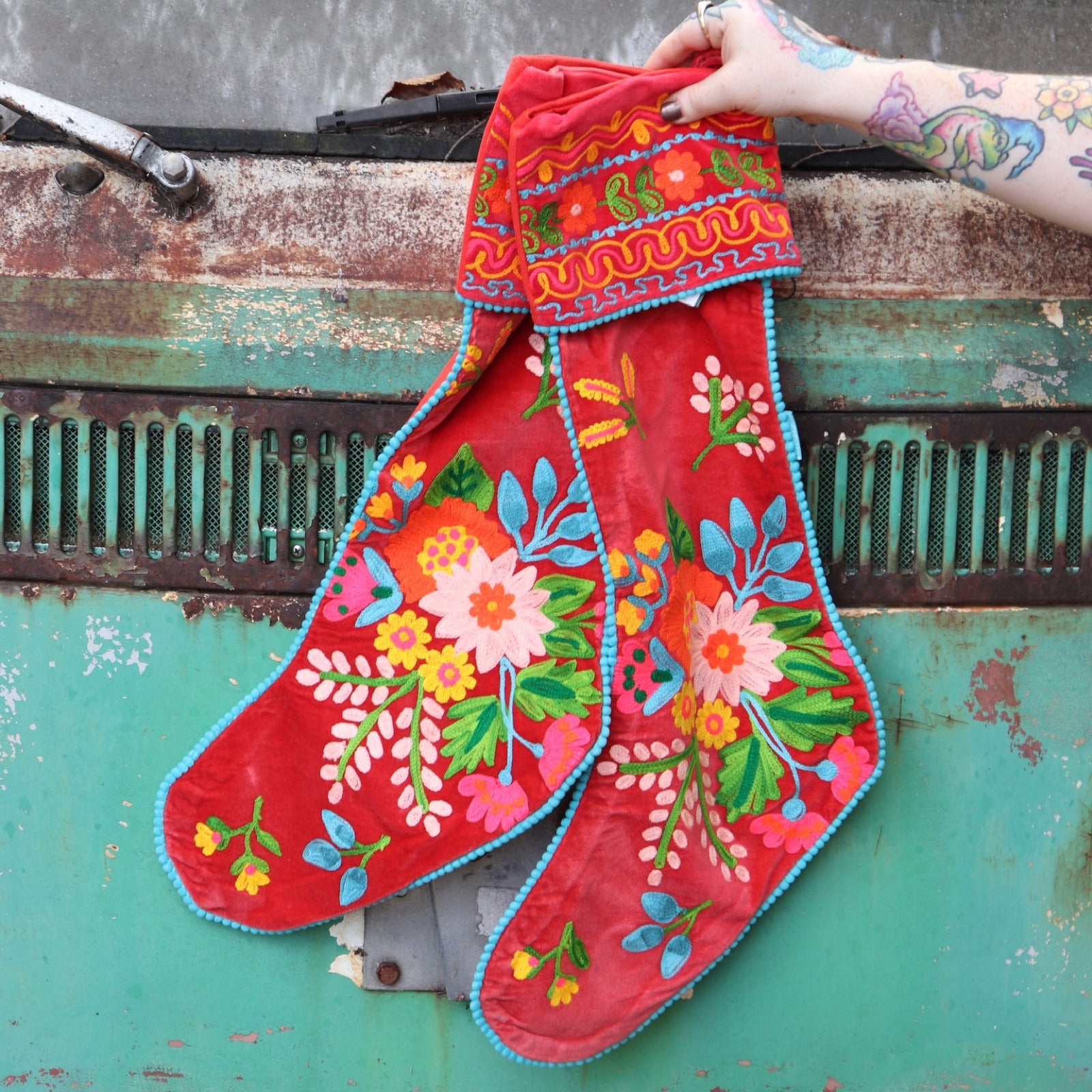 Someone holding the Set of 2 Red Floral Embroidered Stockings in front of a vintage teal Volkswagen bus.