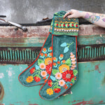 Someone holding the Set of 2 Green Floral Embroidered Stockings in front of a vintage teal Volkswagen bus.