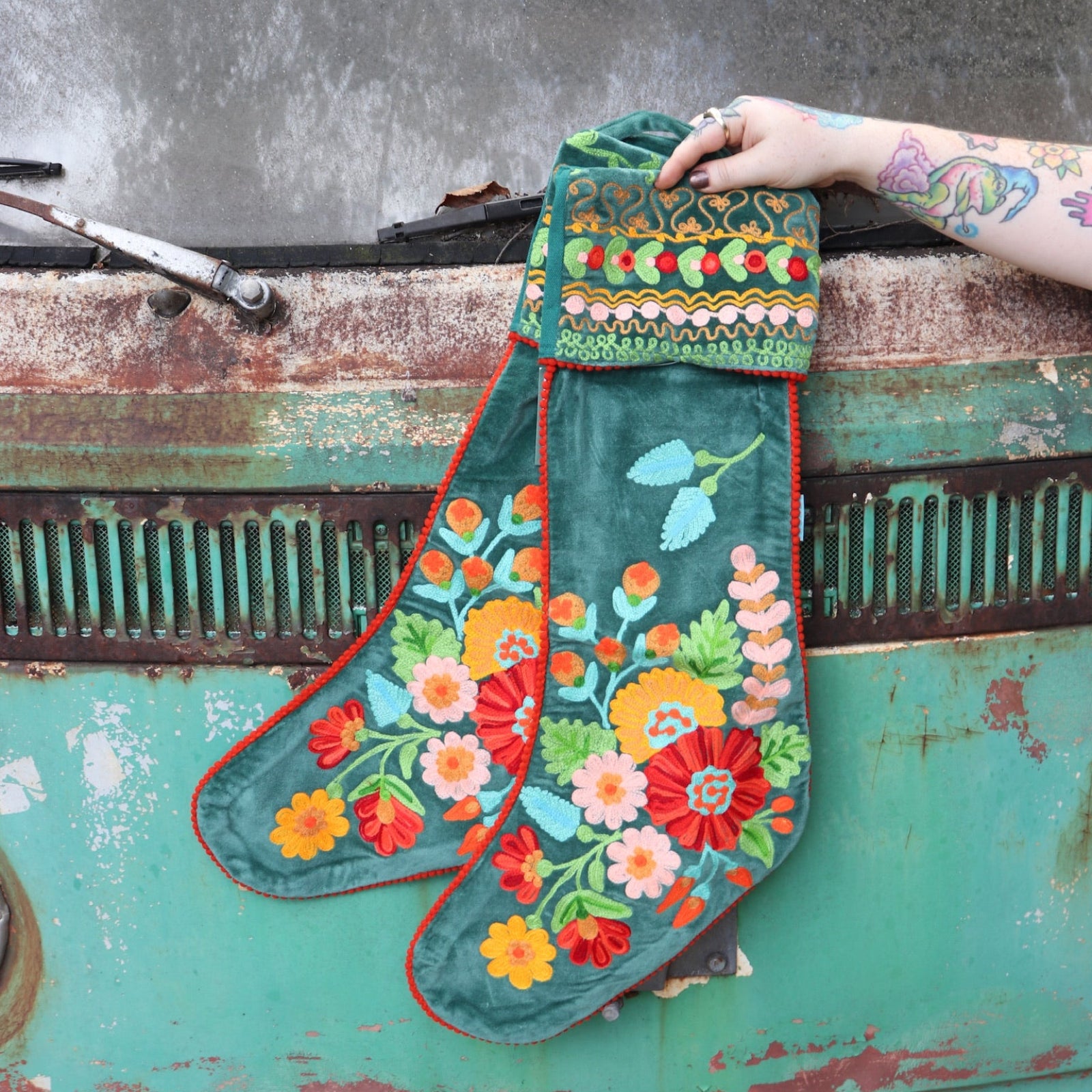 Someone holding the Set of 2 Green Floral Embroidered Stockings in front of a vintage teal Volkswagen bus.