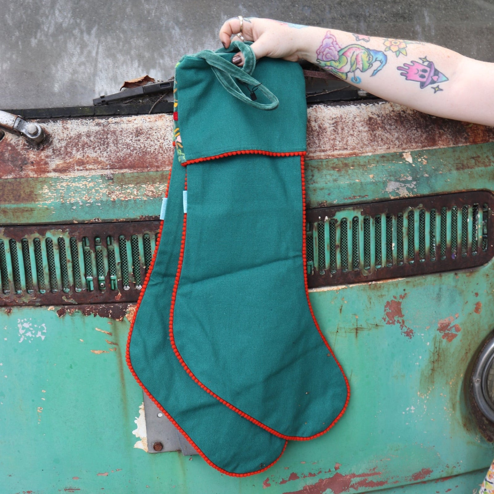 Someone holding the Set of 2 Green Floral Embroidered Stockings in front of a vintage teal Volkswagen bus, showing the back.