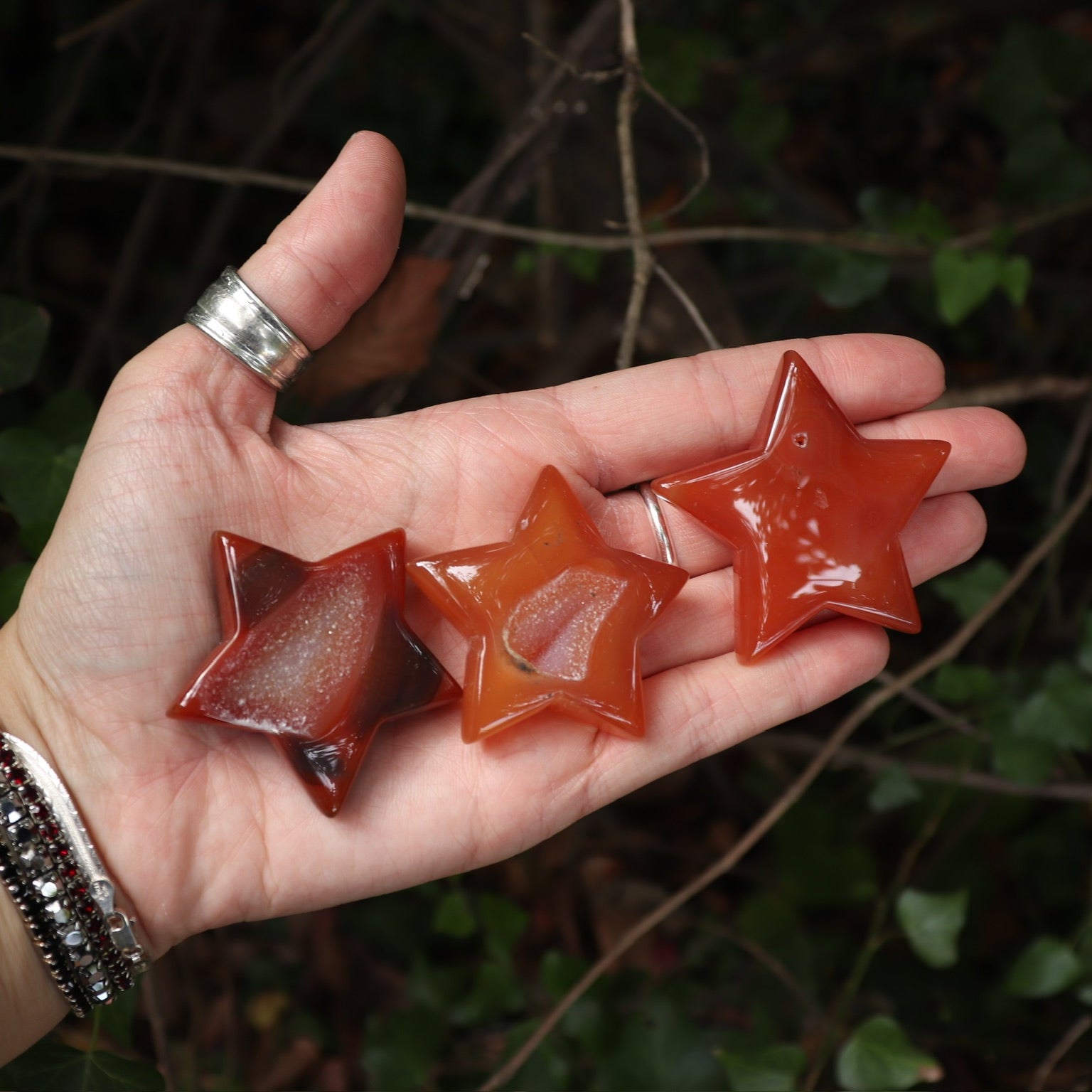 Someone holding three Carnelian Crystal Stars for Confidence & Motivation in front of a green nature background.