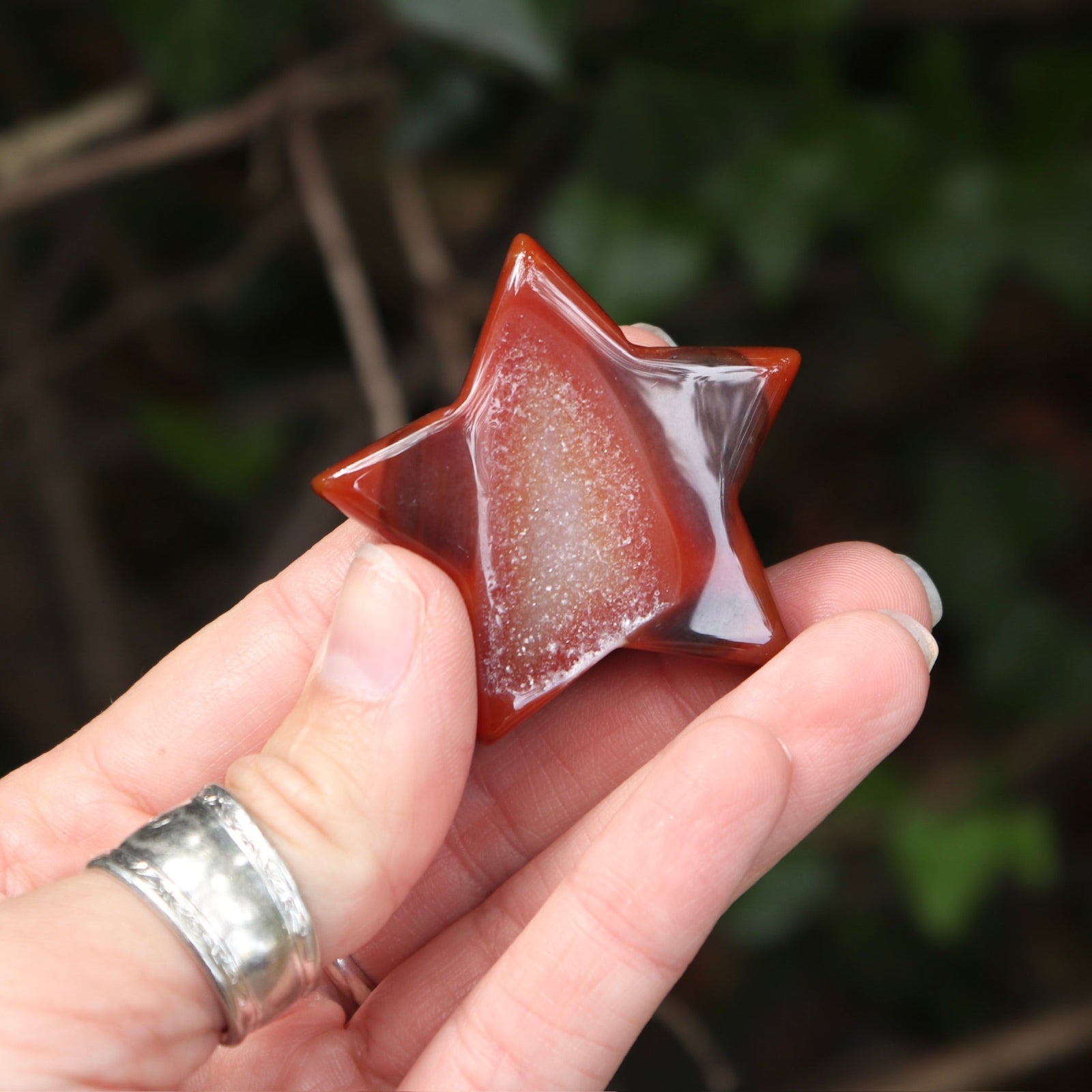 Someone holding a Carnelian Crystal Star for Confidence & Motivation in front of a green nature background.