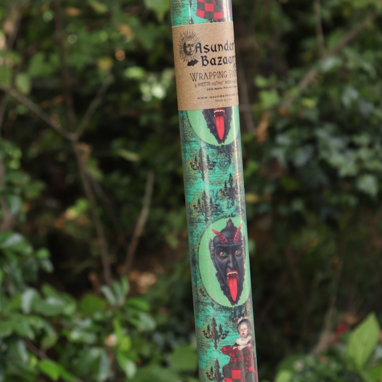 Someone holding the Krampus Children Collage Matte Fine Wrapping Paper in front of greenery.