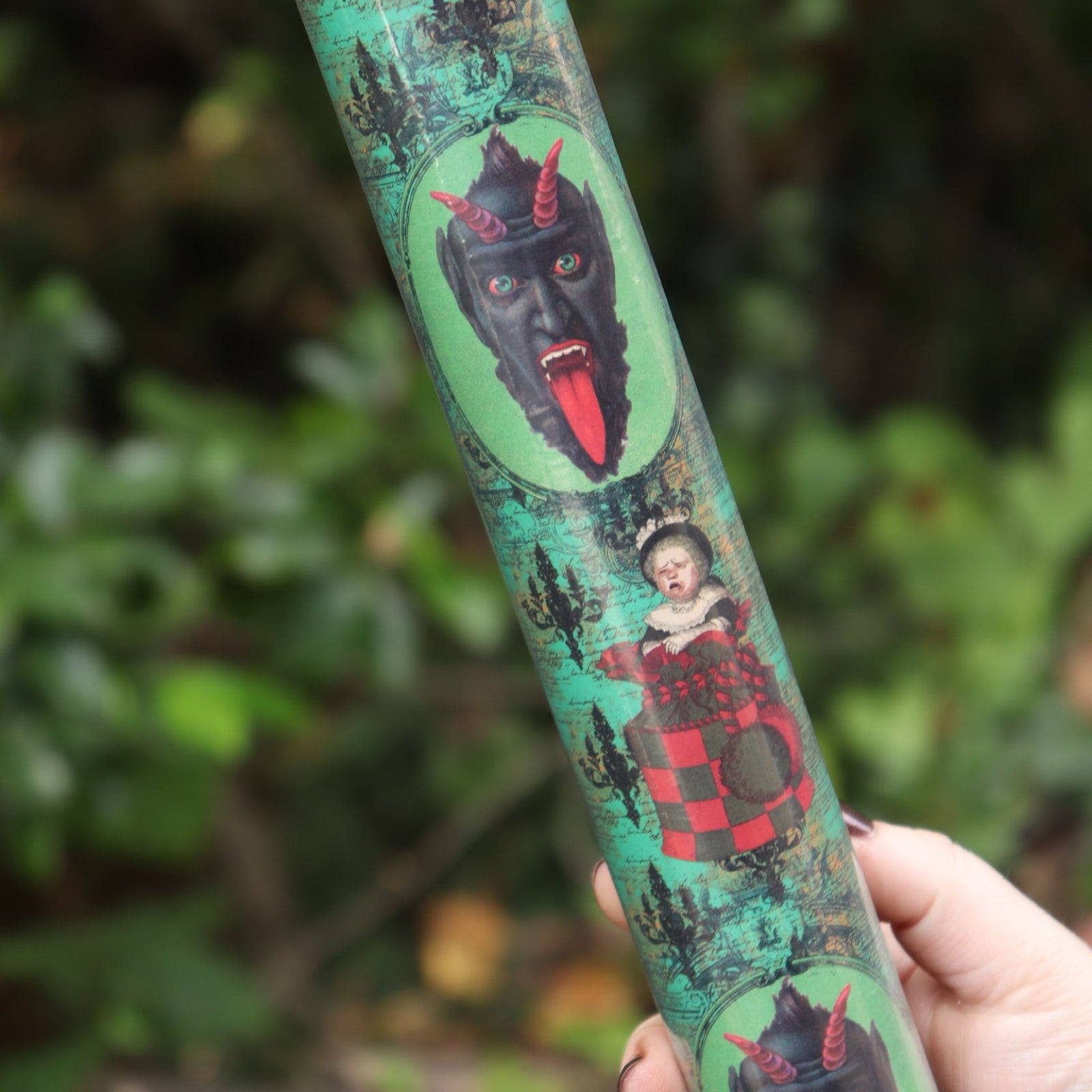 Someone holding the Krampus Children Collage Matte Fine Wrapping Paper in front of greenery.
