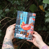 Someone holding the Disco Cocktails Hardcover Book in front of a green bush, showing off the back.