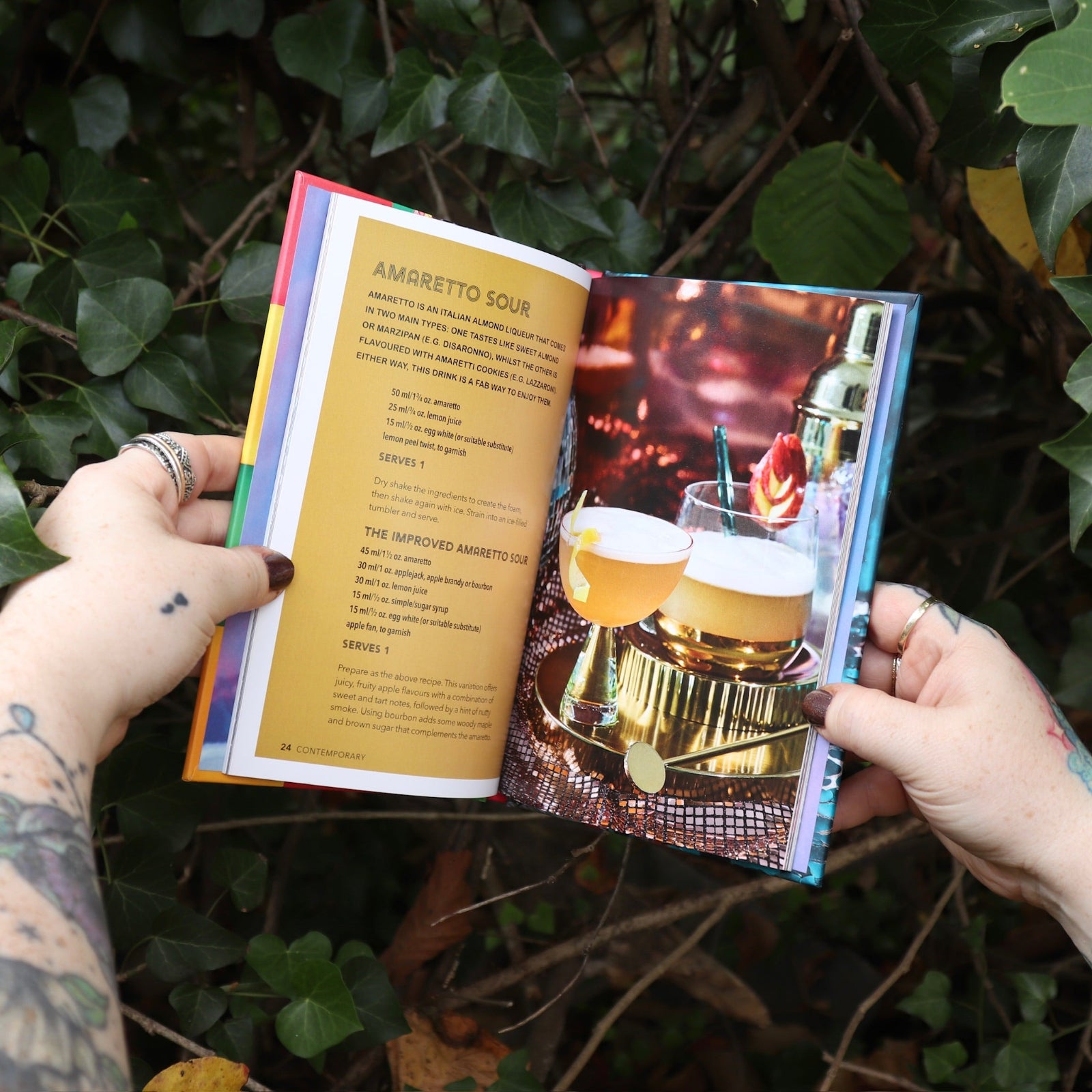 Someone holding the Disco Cocktails Hardcover Book open in front of a green bush.
