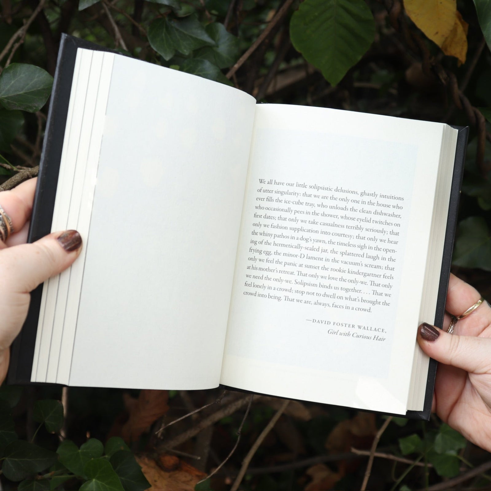 Someone holding the Dictionary of Obscure Sorrows Hardcover Book open in front of a green bush, showing off the pages.