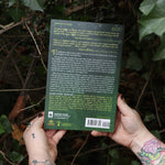 Someone holding the Sacred Herbs of Yule and Christmas in front of a green bush, showing off the back.