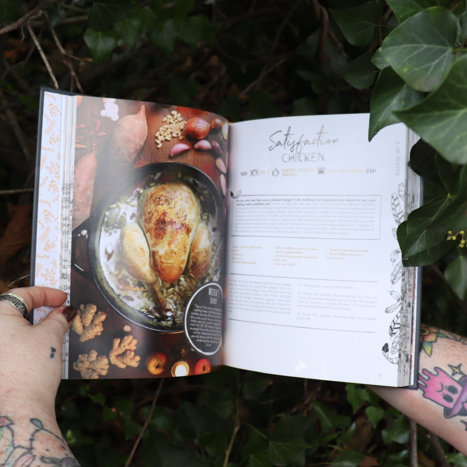 Someone holding the Natural Witch's Cookbook Hardcover Book open in front of a green bush, showing off the pages.