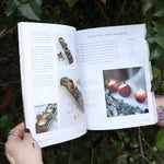 Someone holding the Scandinavian Christmas Crafts Paperback Book open in front of a green bush, showing off the pages.