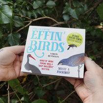 Someone holding the Effin' Birds 2026 Day-to-Day Calendar in front of a green bush.