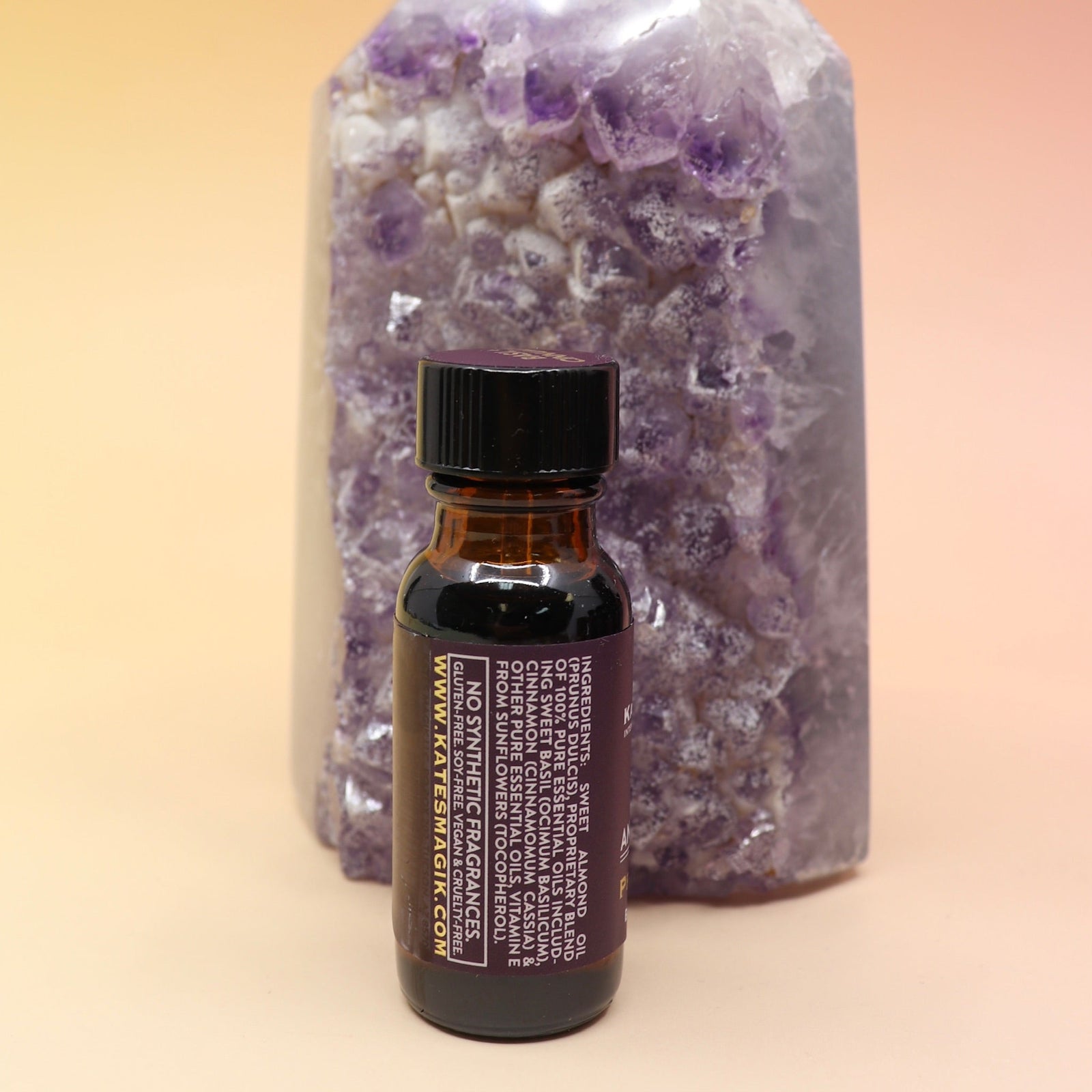 The Prosperity Reiki Charged Anointing Oil in front of an amethyst tower all on a pink and yellow background.