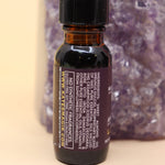 The Letting Go Reiki Charged Anointing Oil in front of an amethyst tower all on a pink and yellow background.