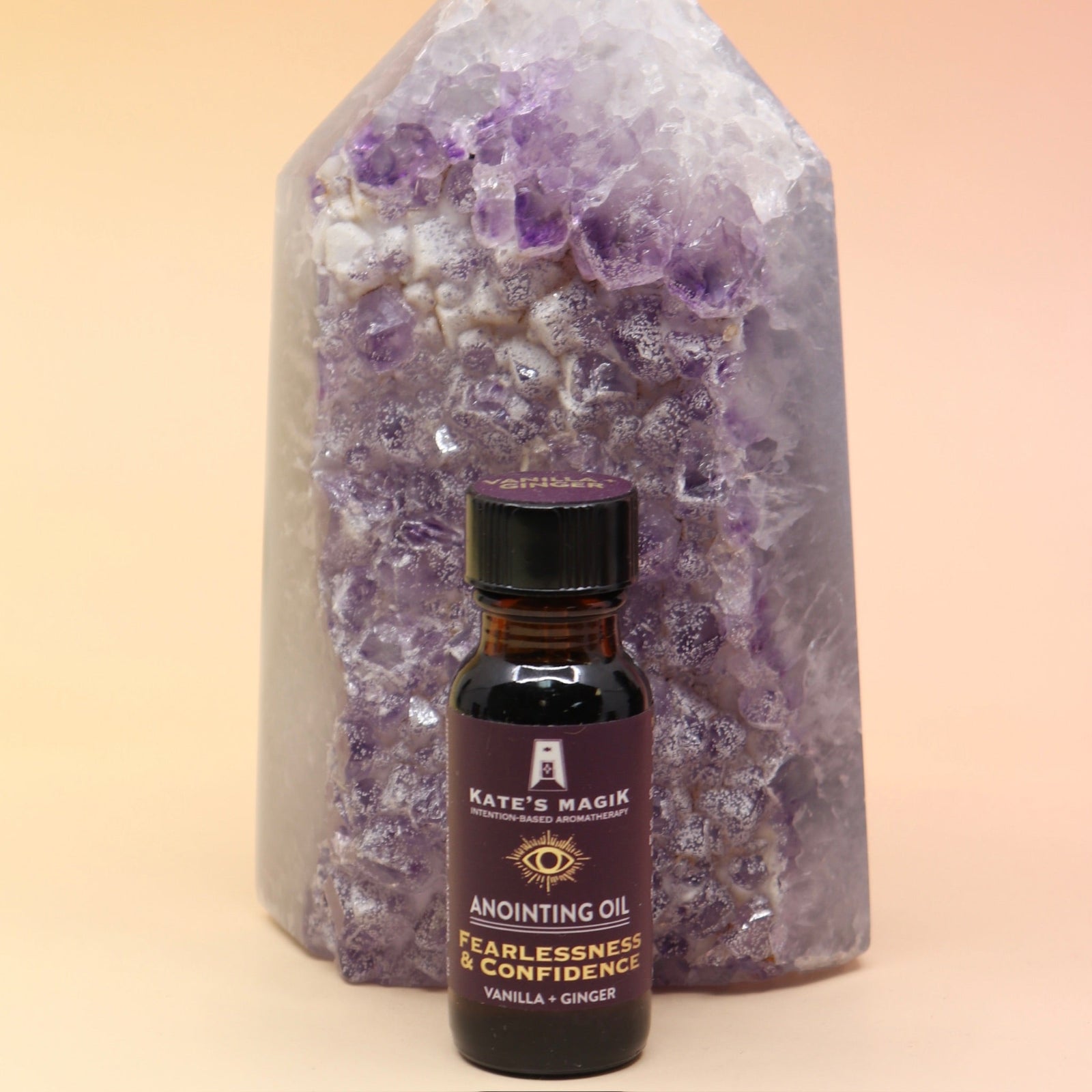The Fearlesssness & Confidence Reiki Charged Anointing Oil in front of an amethyst tower all on a pink and yellow background.