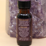 The Fearlesssness & Confidence Reiki Charged Anointing Oil in front of an amethyst tower all on a pink and yellow background.