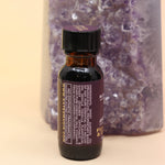 The Fearlesssness & Confidence Reiki Charged Anointing Oil in front of an amethyst tower all on a pink and yellow background.