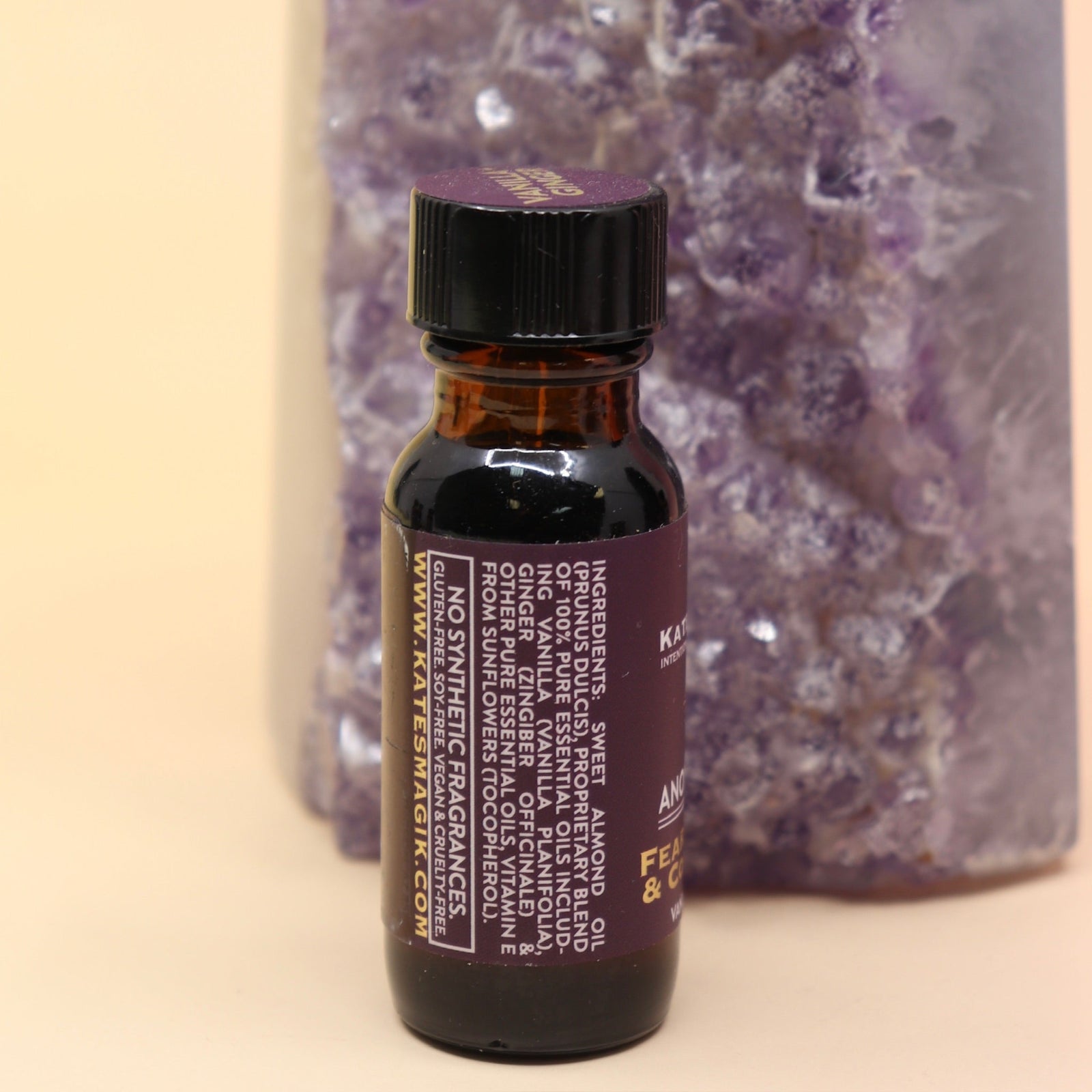 The Fearlesssness & Confidence Reiki Charged Anointing Oil in front of an amethyst tower all on a pink and yellow background.