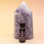 The Healing Reiki Charged Anointing Oil in front of an amethyst tower all on a pink and yellow background.