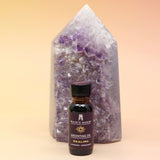 The Healing Reiki Charged Anointing Oil in front of an amethyst tower all on a pink and yellow background.