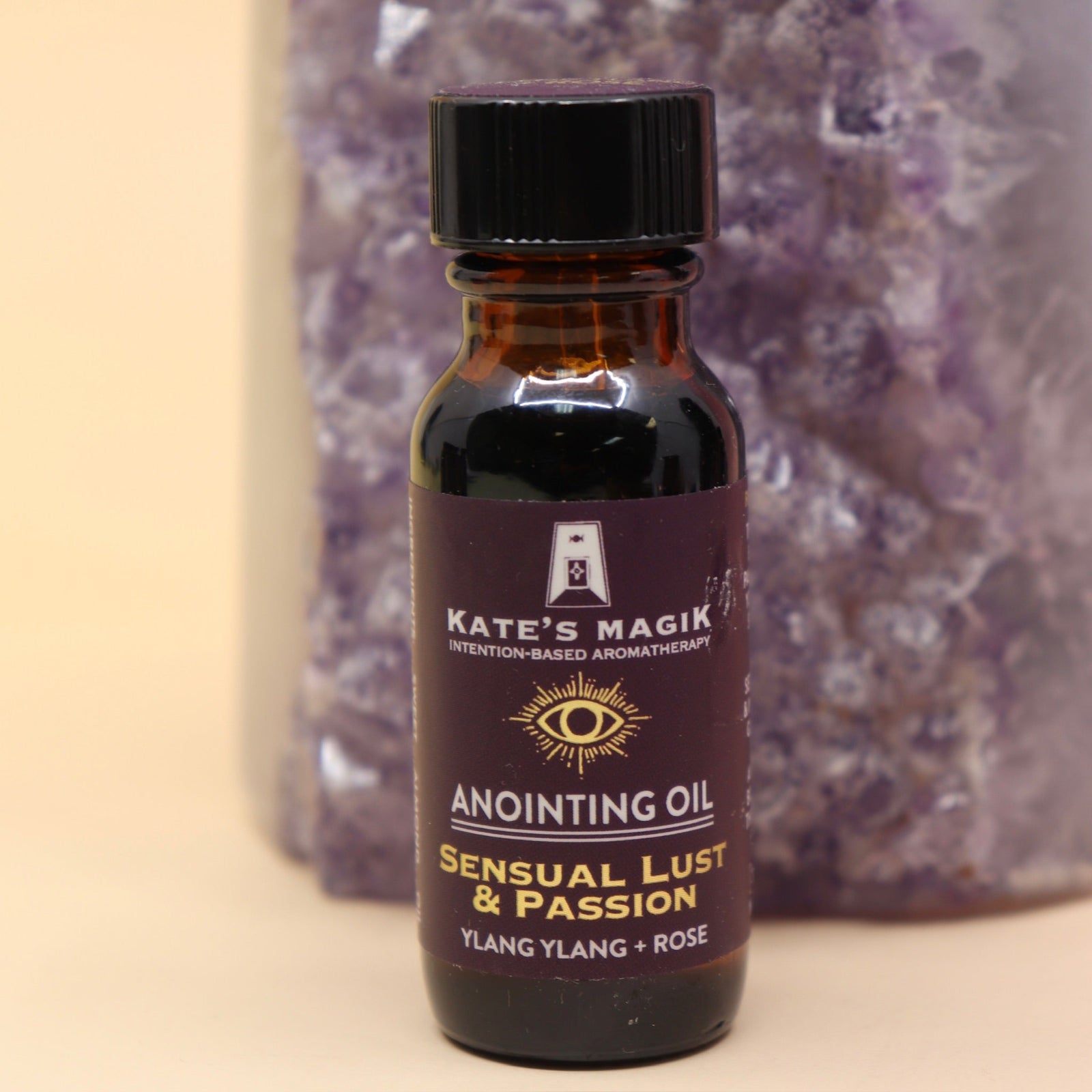 The Sensual Lust & Passion Reiki Charged Anointing Oil in front of an amethyst tower all on a pink and yellow background.