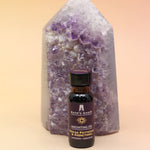 The Break Patterns & Addictions Oil Reiki Charged Anointing Oil in front of an amethyst tower all on a pink and yellow background.