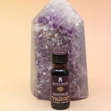 The Break Patterns & Addictions Oil Reiki Charged Anointing Oil in front of an amethyst tower all on a pink and yellow background.