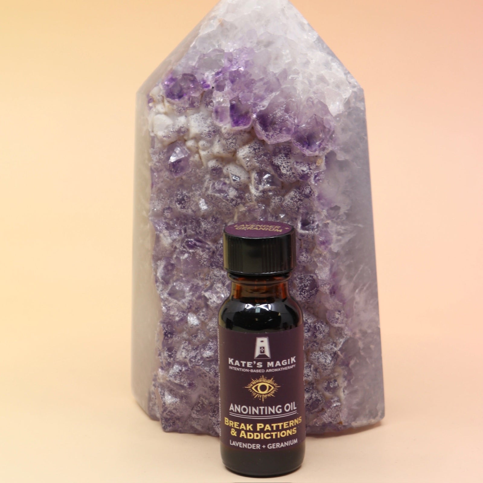 The Break Patterns & Addictions Oil Reiki Charged Anointing Oil in front of an amethyst tower all on a pink and yellow background.