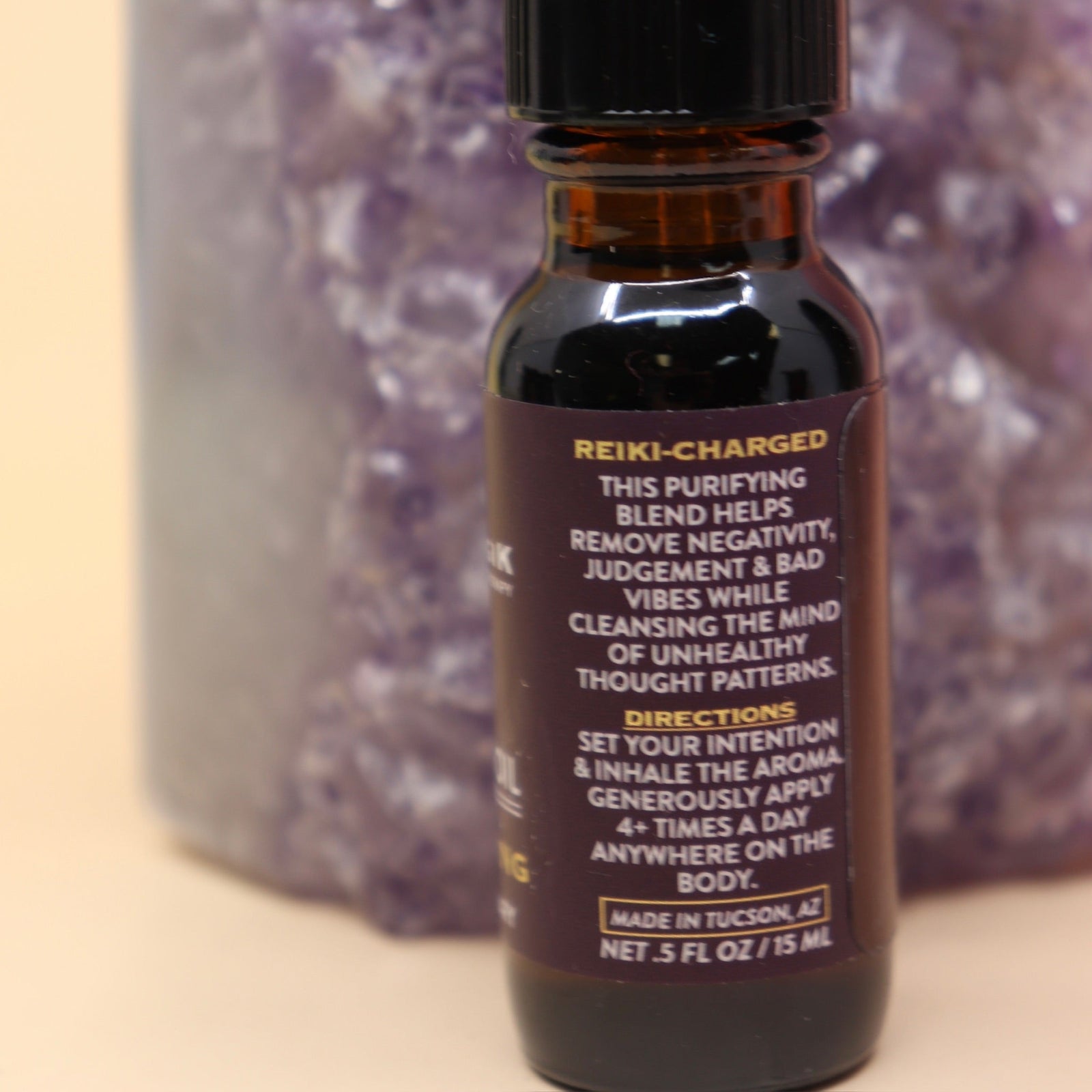 The Uncrossing Oil Reiki Charged Anointing Oil in front of an amethyst tower all on a pink and yellow background.